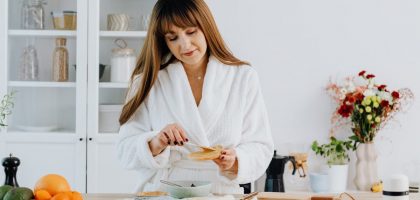 A woman in a bathrobe preparing breakfast in a home kitchen.