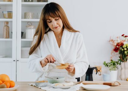 A woman in a bathrobe preparing breakfast in a home kitchen.