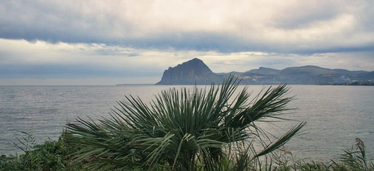 Scenic view of Monte Cofano from Sicilia's coast with lush greenery and calm sea.