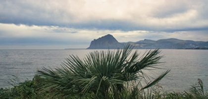 Scenic view of Monte Cofano from Sicilia's coast with lush greenery and calm sea.