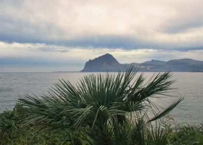 Scenic view of Monte Cofano from Sicilia's coast with lush greenery and calm sea.